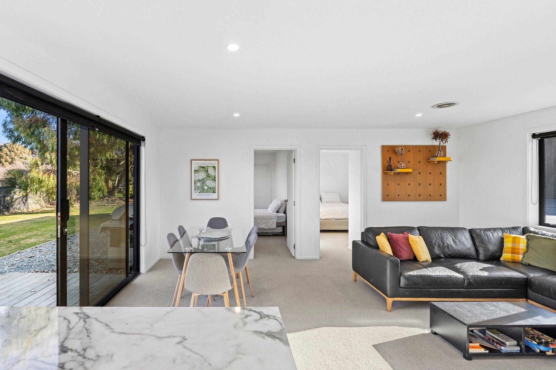 Modern open-plan living room with black leather sofa, marble island, dining table, and glass doors opening to garden