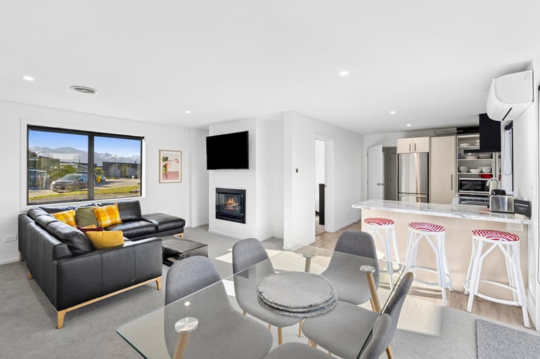 Modern open-concept living room with black leather sofa, yellow cushions, dining area with white bar stools