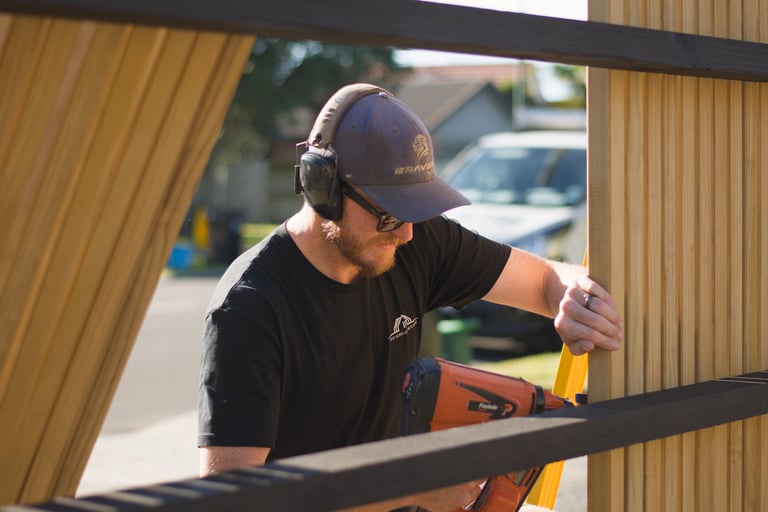 Worker in cap and headphones using level tool on corrugated metal roof panel during construction or installation