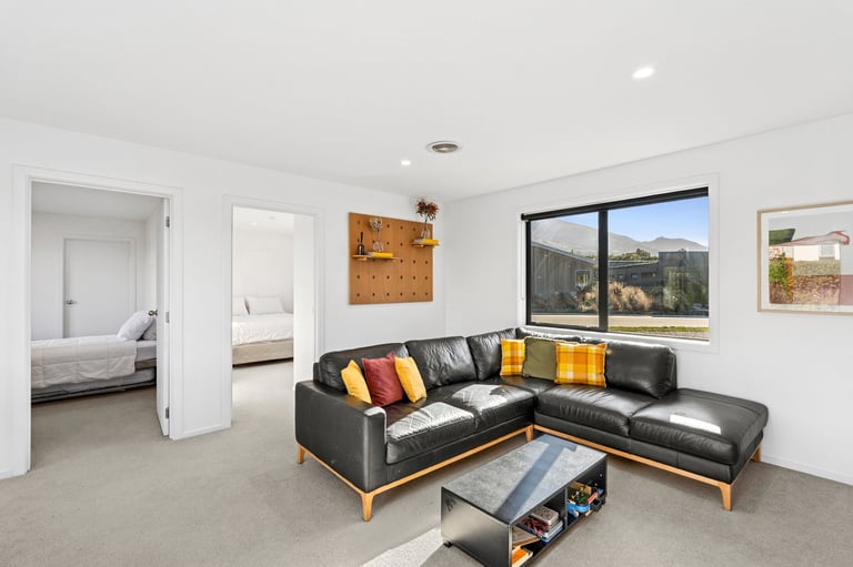 Modern living room with black leather sectional sofa, colorful pillows, glass coffee table