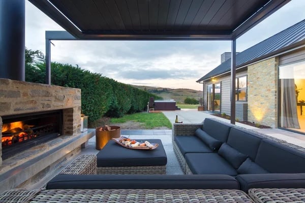 Modern outdoor patio with fireplace, built-in seating, fire pit, and lake view at dusk