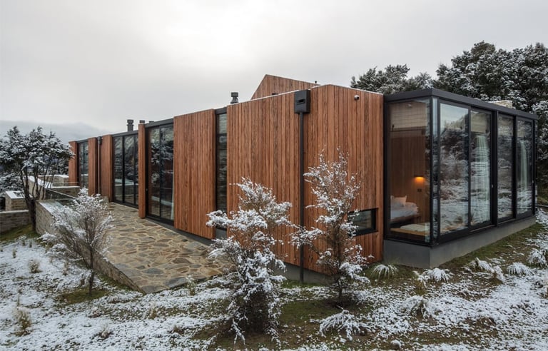 Modern wooden modular house with large windows in snowy landscape with sparse vegetation
