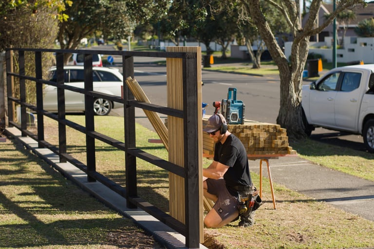 Person working on a black and wood cattle gate in a residential yard on a sunny day